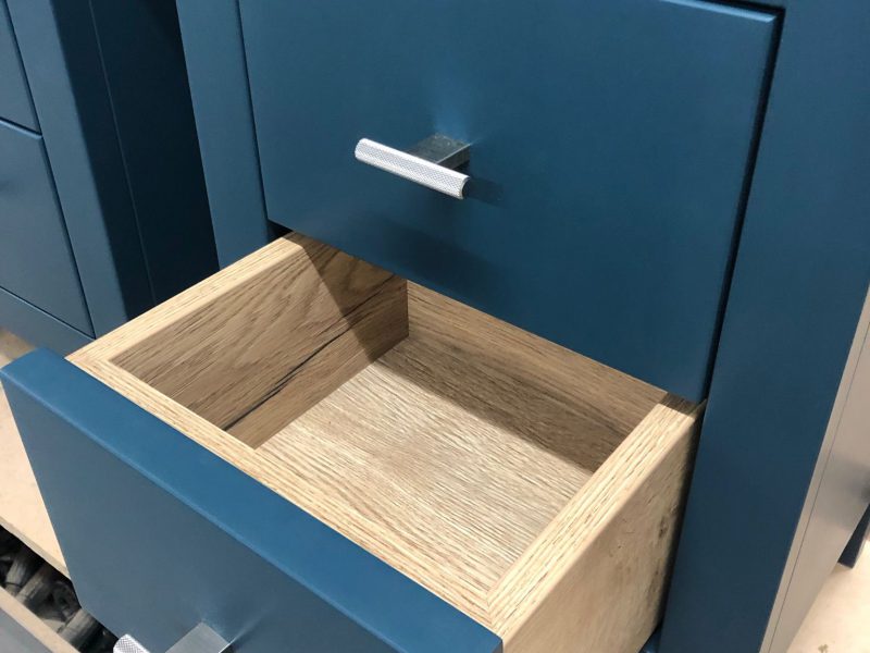 A set of wooden drawers painted in a dusky blue colour. One of the drawers is open. The photograph is shot from an angle.